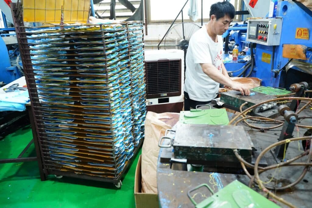 Worker operating molding equipment to produce custom shoe insoles in an insole manufacturing factory.