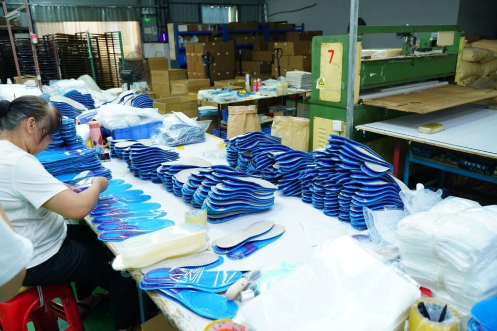 Workers processing and organizing stacks of custom shoe insoles on a factory production line for OEM and ODM manufacturing.